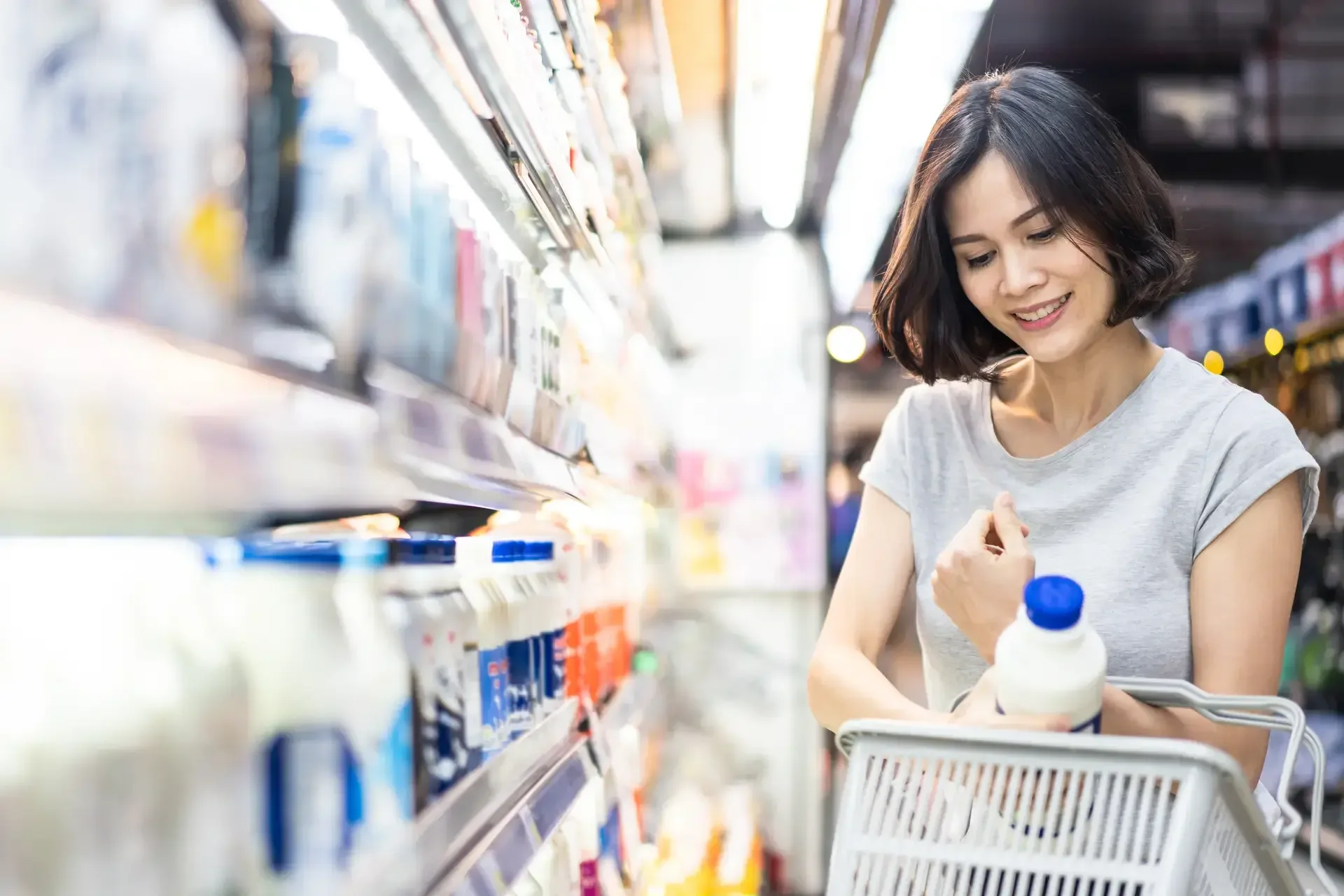 Asyanong babae na nasa grocery linalagay ang isang bote ng gatas sa basket.